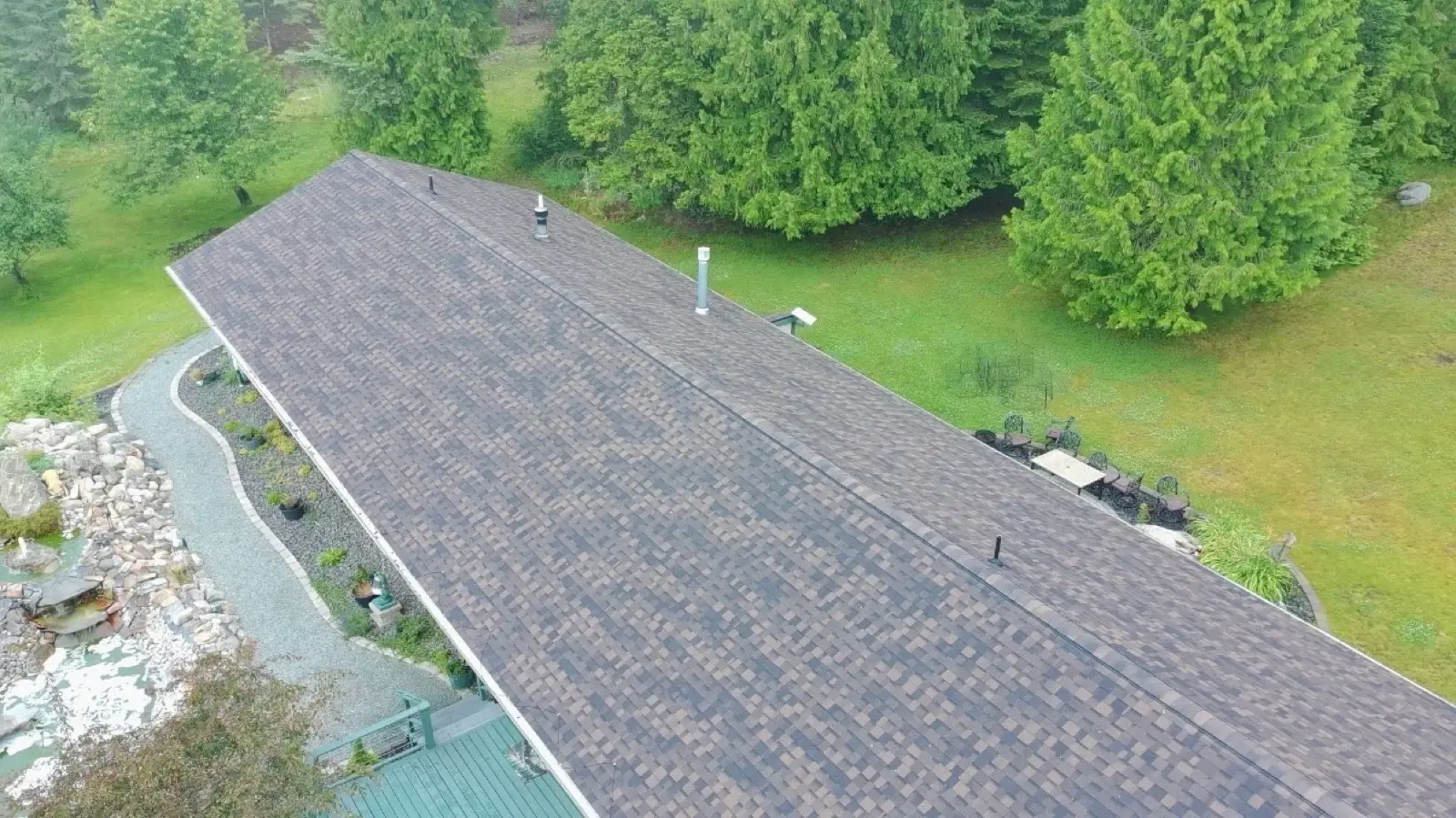 Long weathered-wood shingle roof photographed from above beside a garden pond
